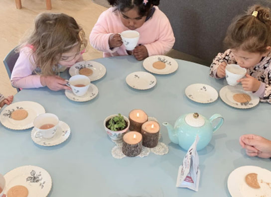 Photo of toddlers gathered at a blue round table eating teas and biscuits